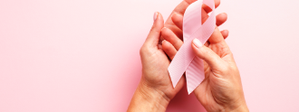 Zwei Hände halten die rosa Brustkrebs-Schleife in der Hand.