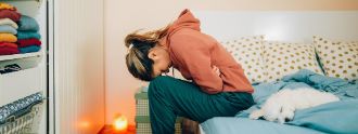 Eine junge Frau sitzt gekrümmt vor Bauchschmerzen auf dem Bett.
