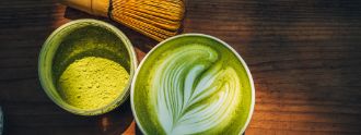 Man sieht einen Becher mit Matcha, sowie einen Matcha Besen und weiteres Zubehör.