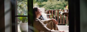 Eine junge Frau sitzt in der Terrassentür und schaut raus.