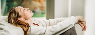 Eine Frau sitzt angelehnt im Bett und sieht erschöpft aus.