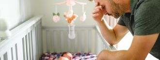 Ein Mann stützt sich auf dem Babybett ab und sieht erschöpft aus.