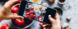 Zwei Hände halten ein Smartphones, durch dessen Kamera man verschiedene Lebensmittel sieht.