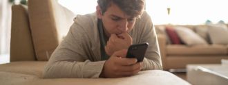 Teenager liegt auf dem Bauch und schaut bedrückt auf sein Handy
