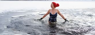 Frau in Badeanzug mit roter Mütze steht im eiskalten Wasser.