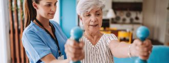 Eine ältere Frau macht Übungen mit Hanteln mit einer Physiotherapeutin. 