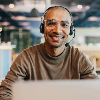Freundlicher Mann sitzt mit Headset und Mikrophon vor seinem Computer in einem Call-Center.