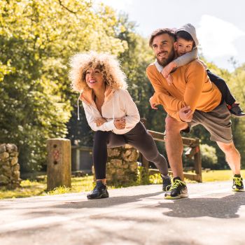 Pärchen mit Kind auf dem Rücken macht Stretching im Park.