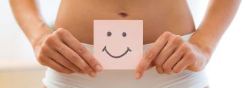 Eine junge Frau hält ein Stück Papier mit einem Smiley drauf über ihren Bauch.