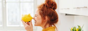Eine Frau mit roten Haaren hält sich lachend ein gelbes Sparschwein vor die Nase.