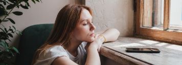 Eine Mädchen sitzt am Fenster und schaut konzentriert auf ein Handy.