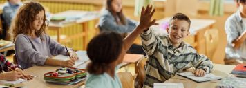 Eine Schulklasse sitzt im Klassenraum und zwei Kinder klatschen sich ab.