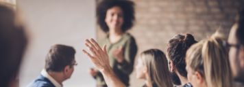 Gruppe von Menschen sitzt an einem Konferenztisch und ein Mann hebt die Hand.