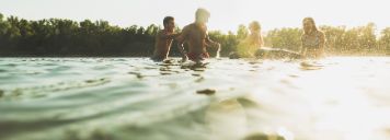 Vier junge Leute baden an einem Sommerabend im See.