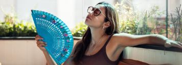 Eine Frau sitzt auf einem Balkon und fächert sich zu.