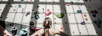 Eine Frau steht vor einer Boulderwand und schaut hoch.