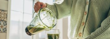 Eine schenkt sich einen grünen Smoothie in ihr Glas.
