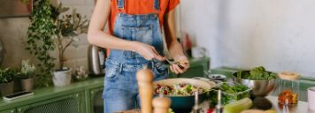 Eine junge Frau steht in der Küche und kocht eine gesunde Mahlzeit.