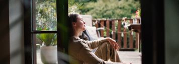 Eine junge Frau sitzt in der Terrassentür und schaut raus.