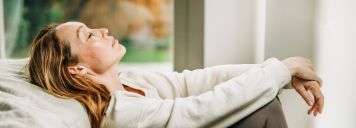 Eine Frau sitzt angelehnt im Bett und sieht erschöpft aus.