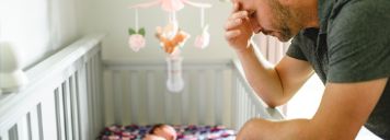 Ein Mann stützt sich auf dem Babybett ab und sieht erschöpft aus.