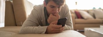 Teenager liegt auf dem Bauch und schaut bedrückt auf sein Handy