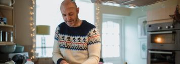 Ein Mann im Weihnachtspullover steht in der Küche und kocht.