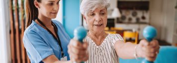 Eine ältere Frau macht Übungen mit Hanteln mit einer Physiotherapeutin. 