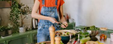 Eine junge Frau steht in der Küche und kocht eine gesunde Mahlzeit.