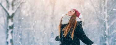 Junge Frau mit langen Haaren in Winterkleidung genießt den Schnee.