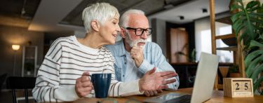 Ein älteres Paar sitzt vor dem Laptop und plant Termine.