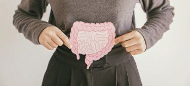 Eine Frau hält ein Modell eines Darms mit beiden Händen vor ihren Bauch, es symbolisiert Darmgesundheit.
