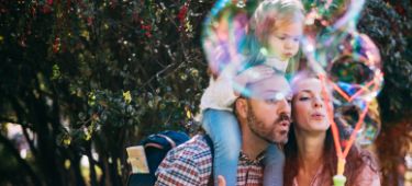 Ein Mann, ein Baby und eine Frau liegend als Familie auf einer Decke.
