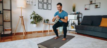 Mann macht Sportübungen auf einer Matte im Wohnzimmer.