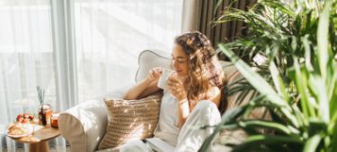 Eine junge Frau sitzt auf einem Sessel und genießt ihren Tee.