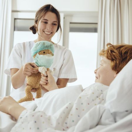 Ein Junge liegt im Krankenhausbett und die Ärztin gibt ihm einen Teddy.