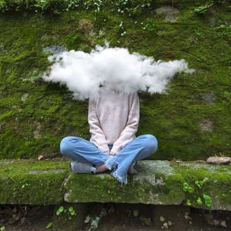 Jugendliche sitz vor einer mit Moss bedeckten Mauer und hat eine Wolke um den Kopf.