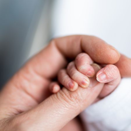 Eine erwachsene Hand hält die Hand eines Neugeborenen.