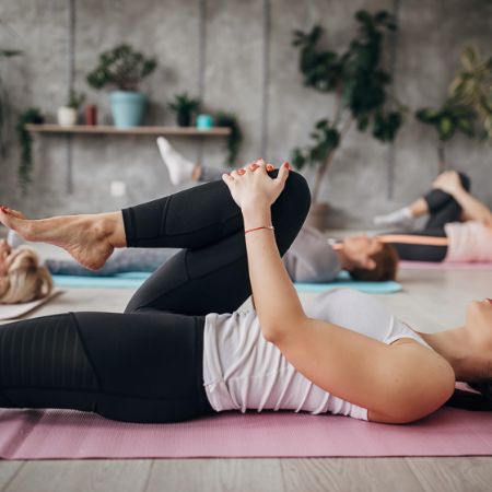Frauen liegen auf einer Sportmatte und machen eine Pilates-Übung.