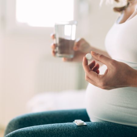 Eine schwangere Frau nimmt eine Tablette mit einem Glas Wasser ein.