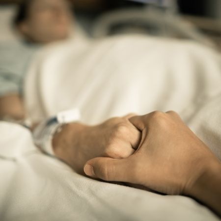 Die Hand einer jungen Person hält die Hand einer alten Person, die in einem Krankenhausbett liegt