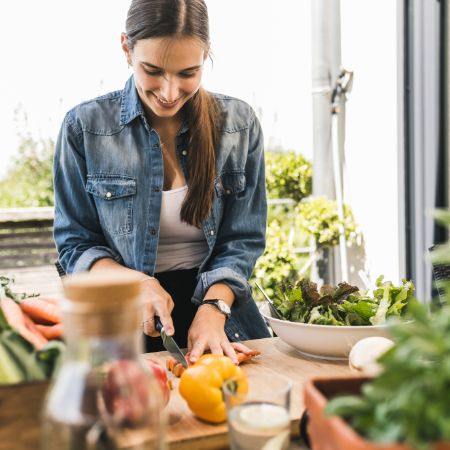Eine junge Frau schneidet auf ihrem Balkon eine Paprika.