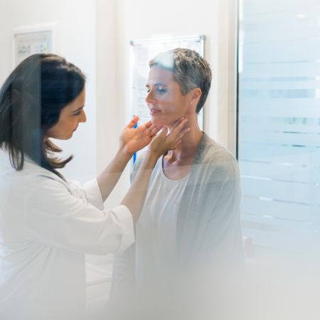 Eine Ärztin tastet die Schilddrüse einer Patientin ab.