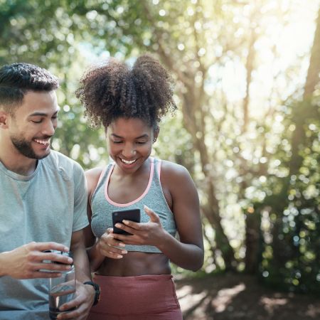 Mann und Frau in Sportklamotten schauen auf ein Handy.