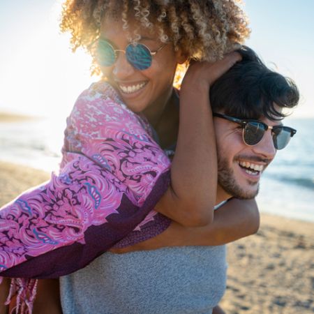 Mann trägt Frau huckepack am Strand.
