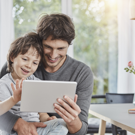 Ein Vater schaut mit seinem kleinen Sohn lächelnd auf eine Tablet.
