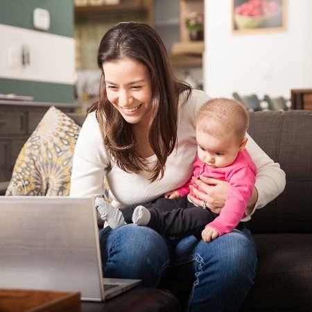 Frau sitzt lächelnd mit Baby vor dem Laptop.