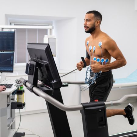 Ein junger Mann läuft auf einem Laufband und lässt ein Belastungs-EKG durchführen.