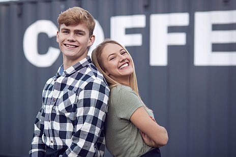 Junger Mann und junge Frauen stehen Rücken an Rücken und lächeln.